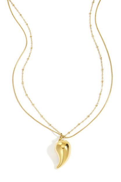 Gold layered necklace with a smooth curved droplet pendant and mixed delicate chains on a white background