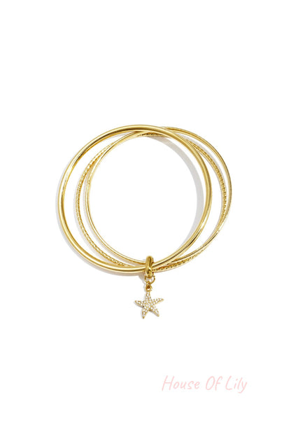 Two gold-tone bangles with a starfish charm adorned with rhinestones on a white background