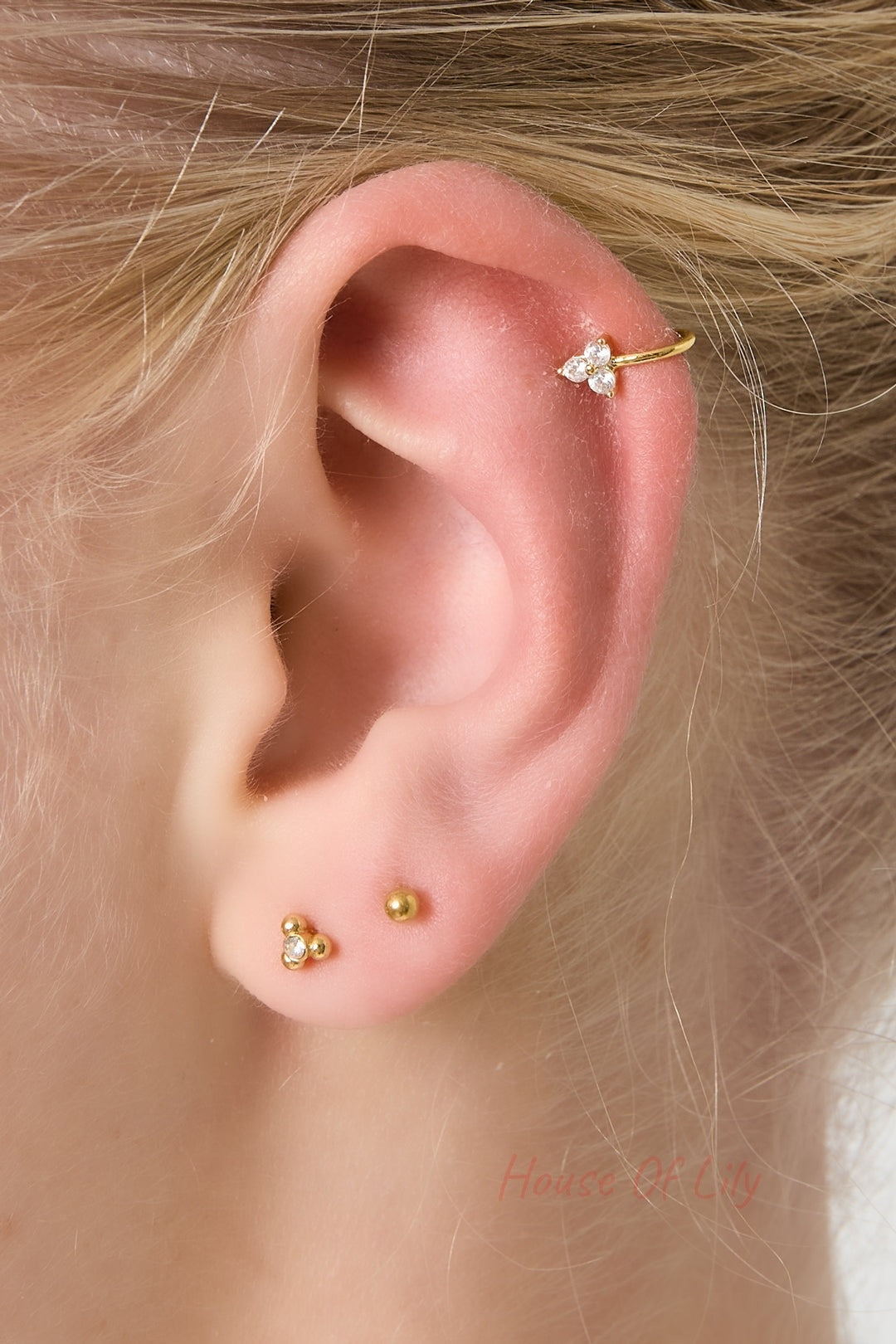 Close-up of a woman's ear adorned with the gold ear cuff and small stud earrings, featuring three zircon stones