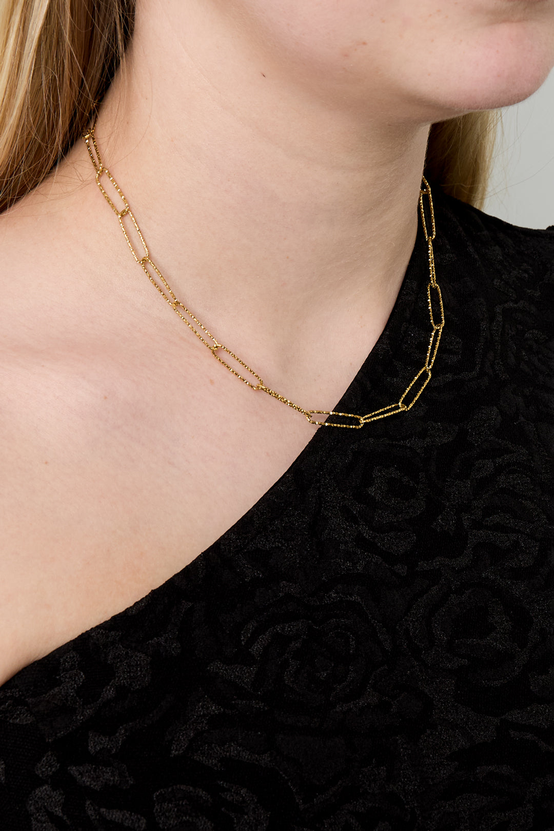 Close-up of woman wearing gold paperclip chain necklace without pendant on black top