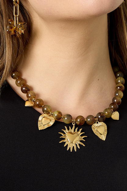 Close-up of model's neck showing amber brown beads and gold sun and heart charms on necklace
