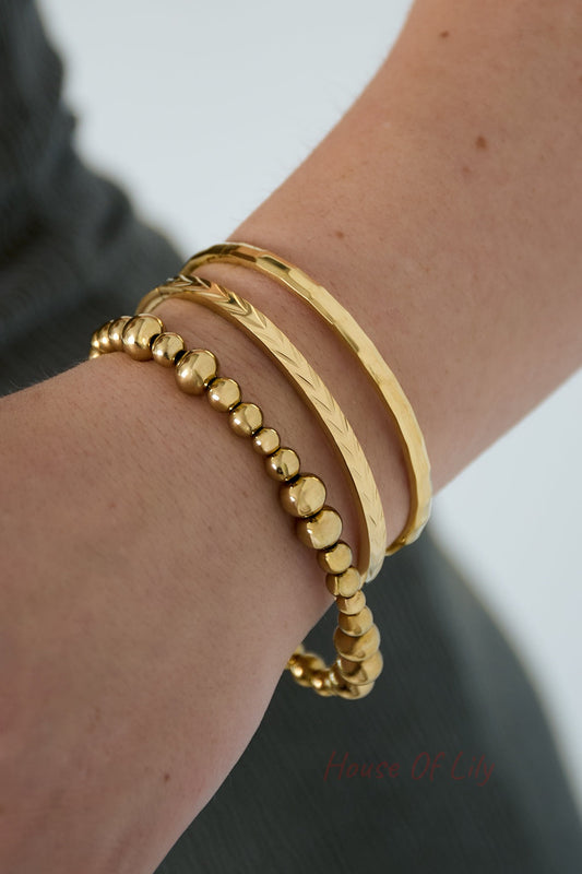 Close-up of a wrist wearing three gold bangles including geometric faceted bangle, textured band, and beaded bracelet