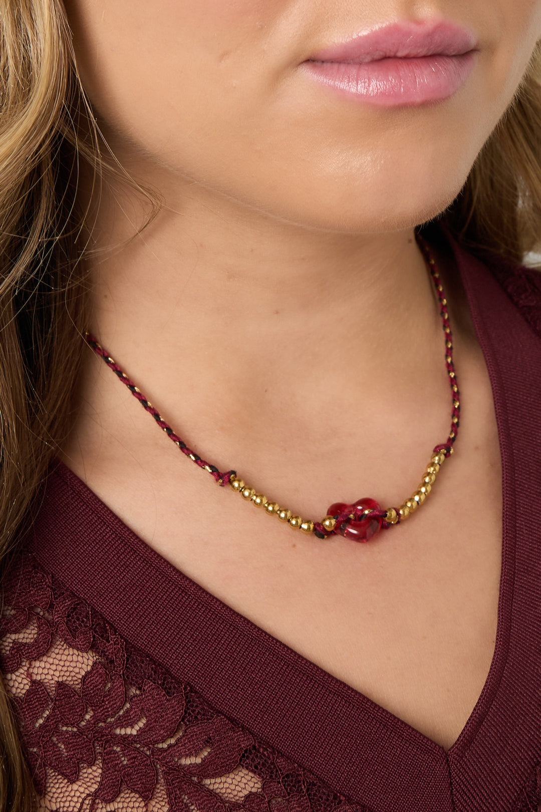 Close-up of woman's neckline wearing the burgundy braided necklace with red heart bead and gold-tone beads