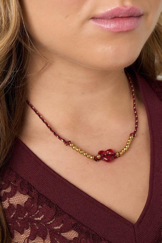 Close-up of woman's neckline wearing the burgundy braided necklace with red heart bead and gold-tone beads