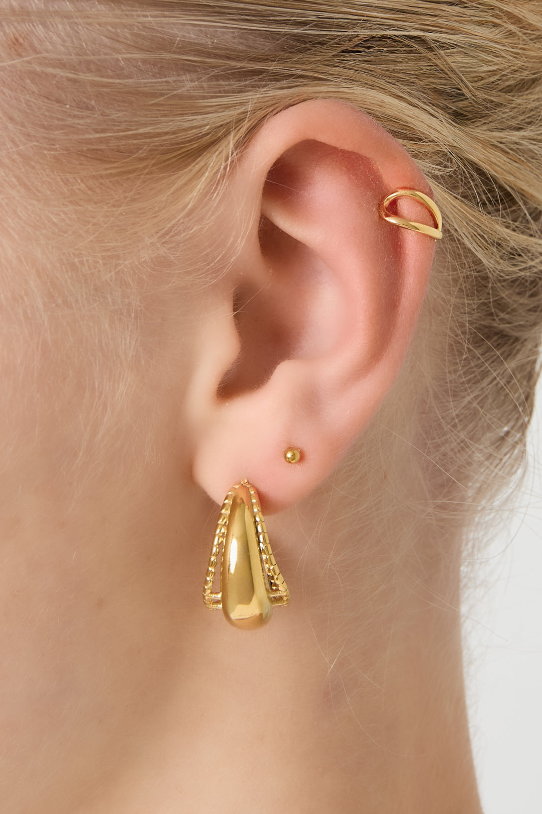 Close-up of a woman wearing a gold double loop ear cuff on upper ear with gold earrings below