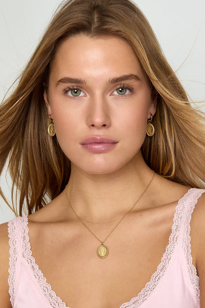 Front view of woman wearing gold floral oval hoop earrings and matching necklace