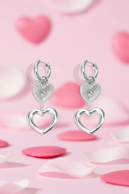 Pair of silver-toned heart charm hoop earrings with layered heart pendants on a white background