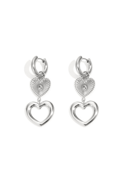 Silver hoop dangle earrings featuring a textured starburst heart charm above an open heart silhouette.