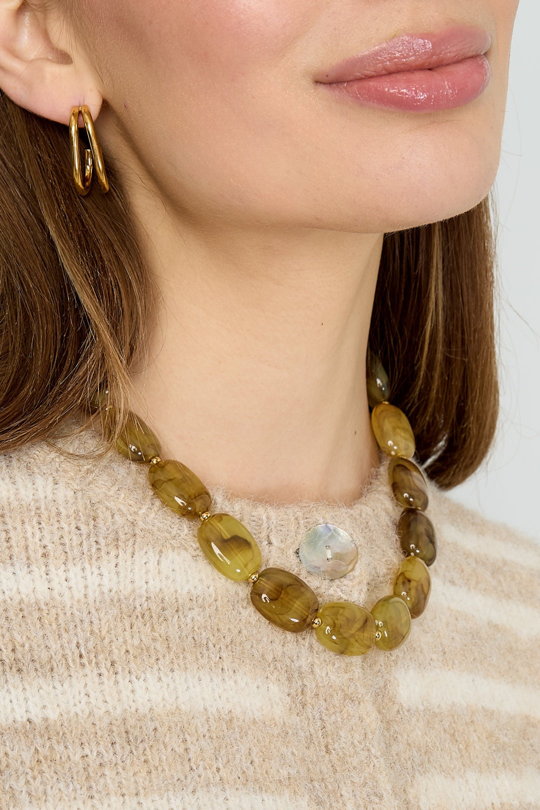 Detailed side view of amber marbled acrylic bead necklace worn by model in cozy knit sweater
