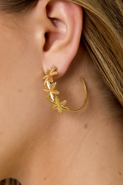 Close-up of gold floral hoop earring worn on a woman's ear with blonde hair
