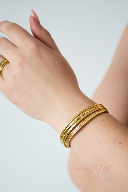 Close-up of a woman wearing stacked gold bangles including the slim rhinestone-accented bangle