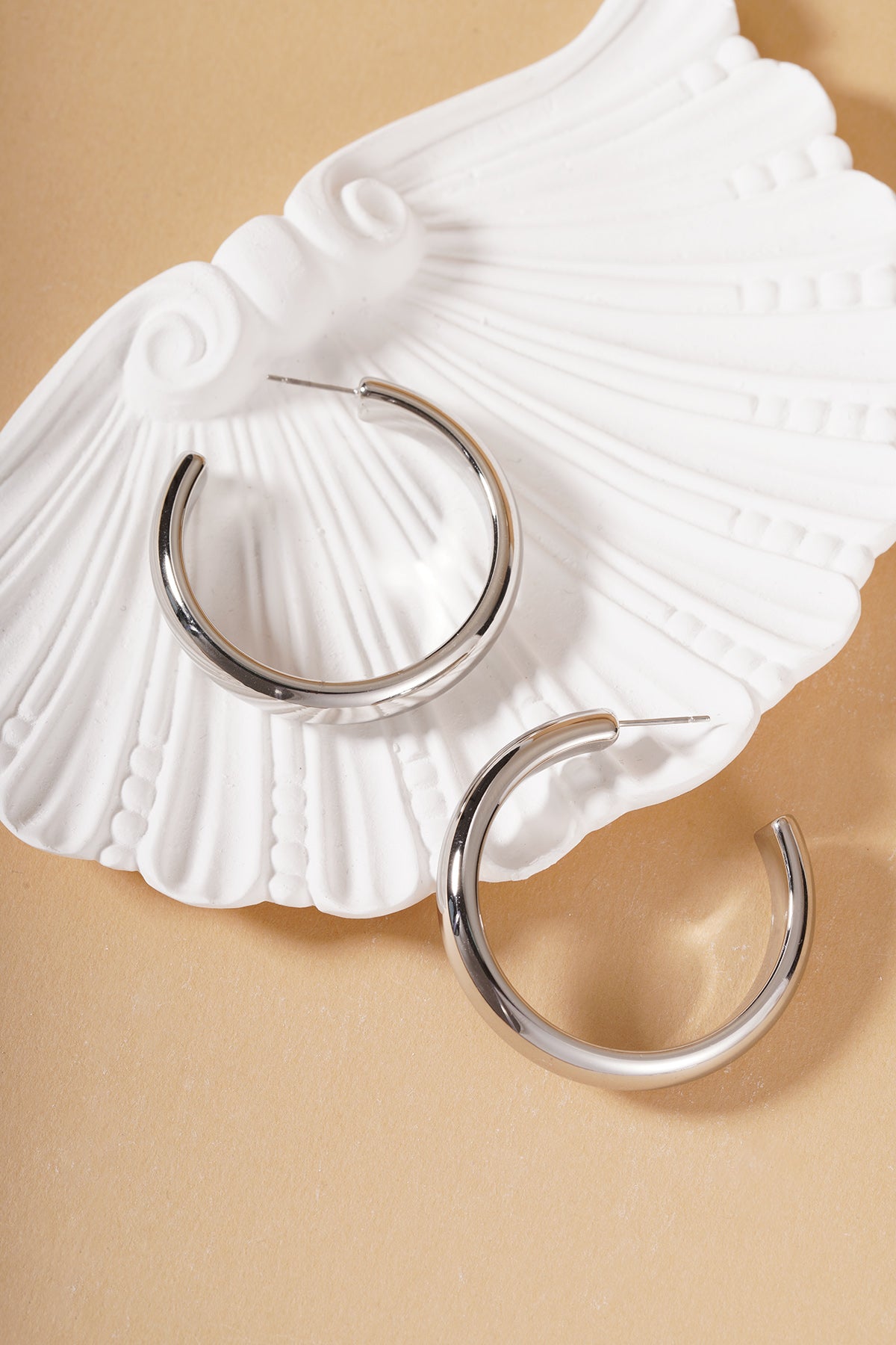 Silver chunky hoop earrings displayed on a decorative white shell plate on a neutral surface