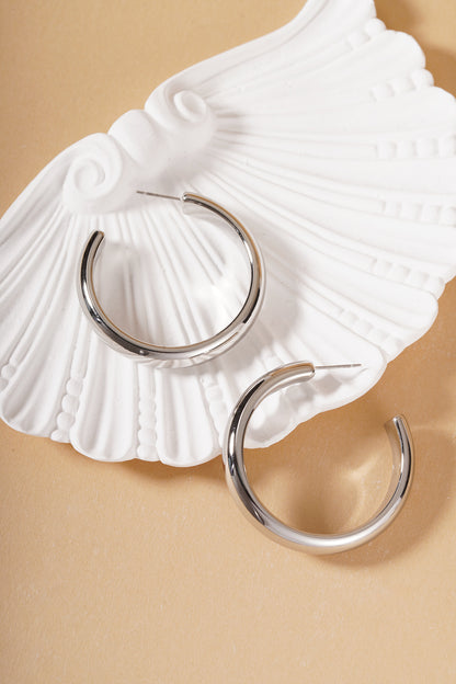 Silver chunky hoop earrings displayed on a decorative white shell plate on a neutral surface
