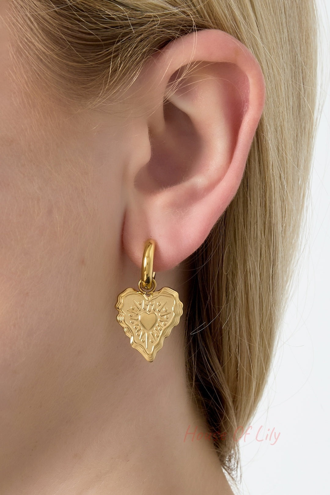 Gold heart charm hoop earring worn on a woman’s ear, showing size and fit