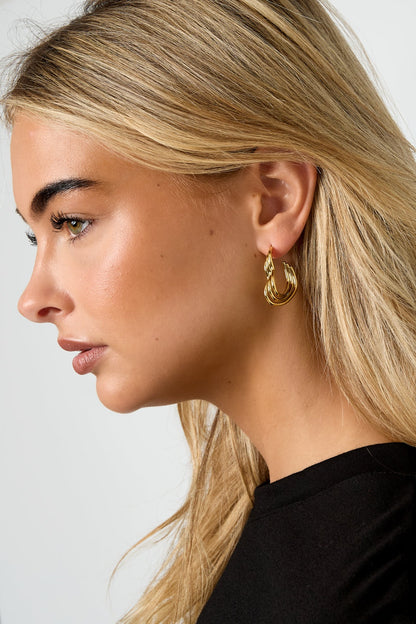 Close-up side profile of a woman wearing gold heart-shaped ribbed hoop earrings with black top