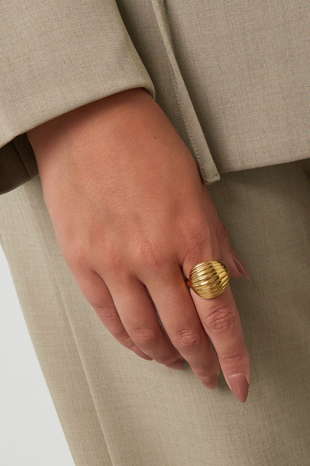 Close-up of woman wearing gold ribbed statement ring with beige outfit