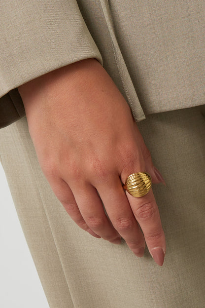 Close-up of woman wearing gold ribbed statement ring with beige outfit
