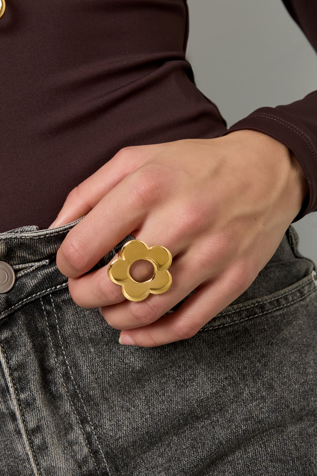 Model wearing gold flower statement ring with dark top and gray jeans close-up