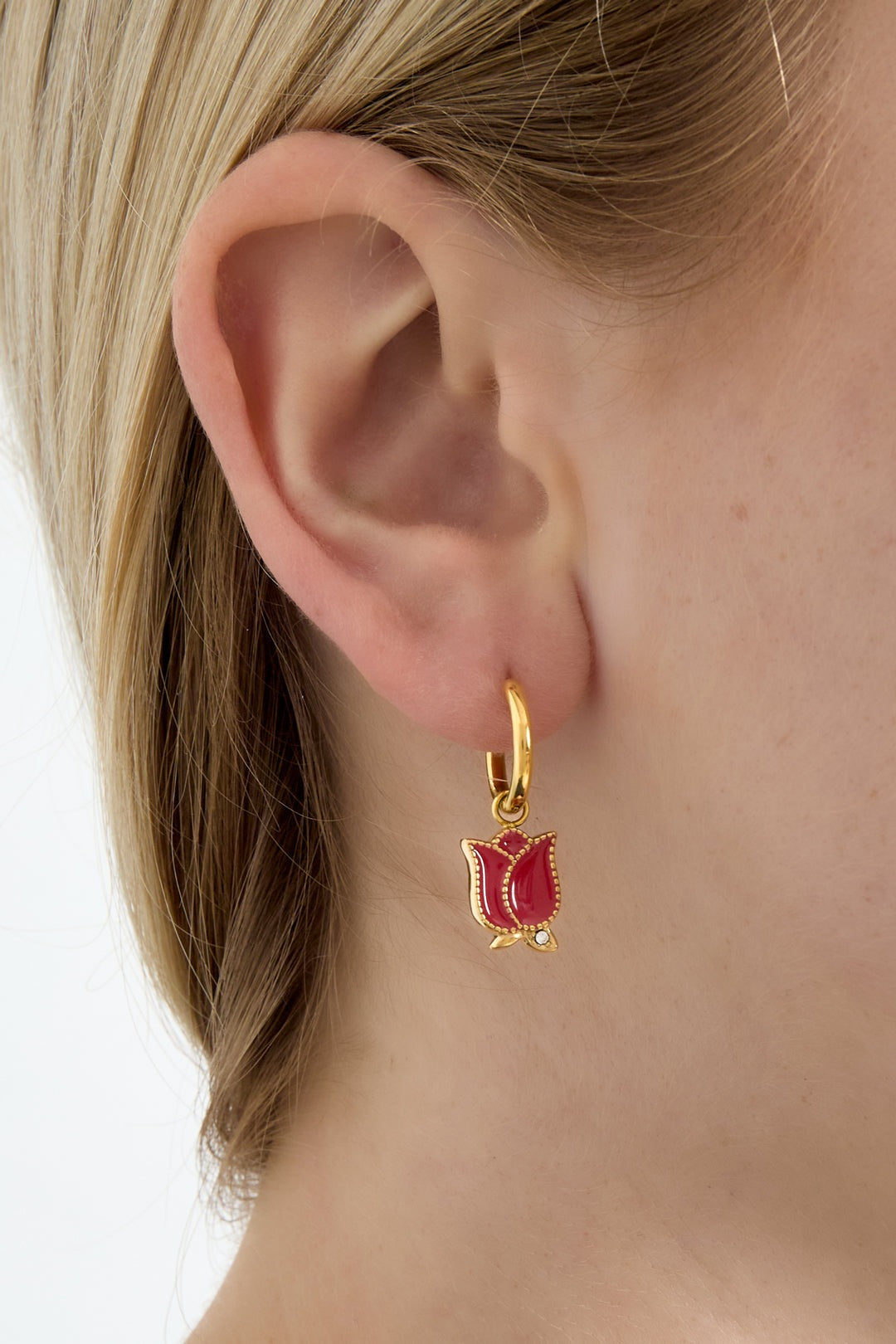 Close-up of woman wearing gold hoop earrings with red enamel tulip flower charms