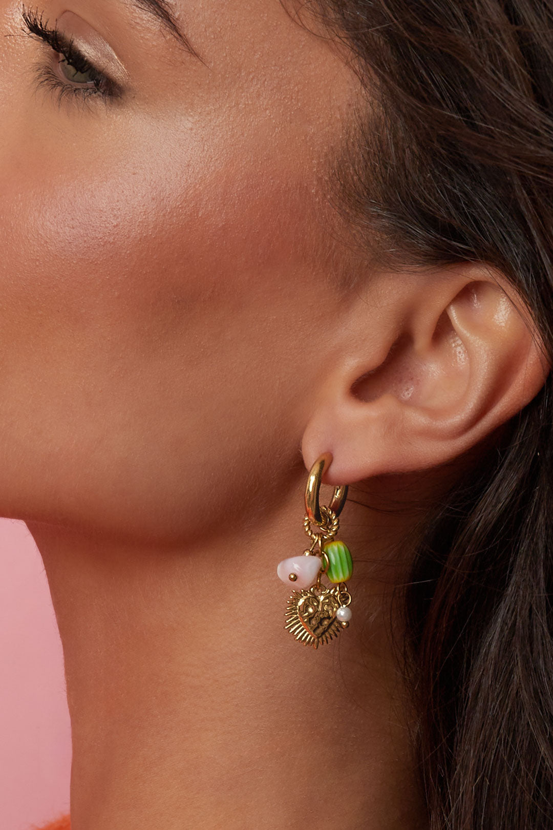 Close-up view of the gold-tone heart dangle earring on model's ear highlighting the detailed heart pendant and colorful beads