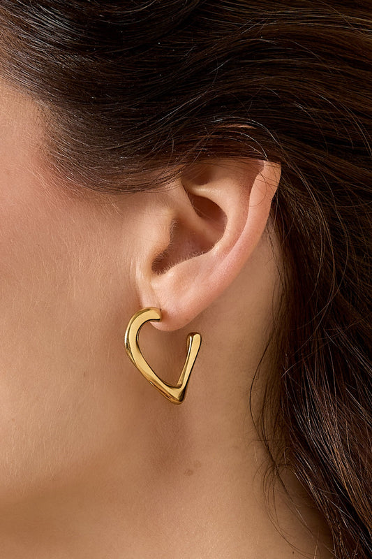 Close-up of gold heart hoop earring on model's ear showcasing smooth, reflective metal and unique open-heart shape