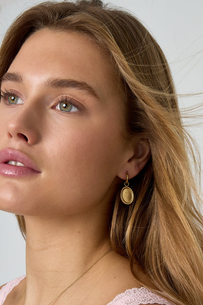 Side profile of woman wearing gold floral oval hoop earring