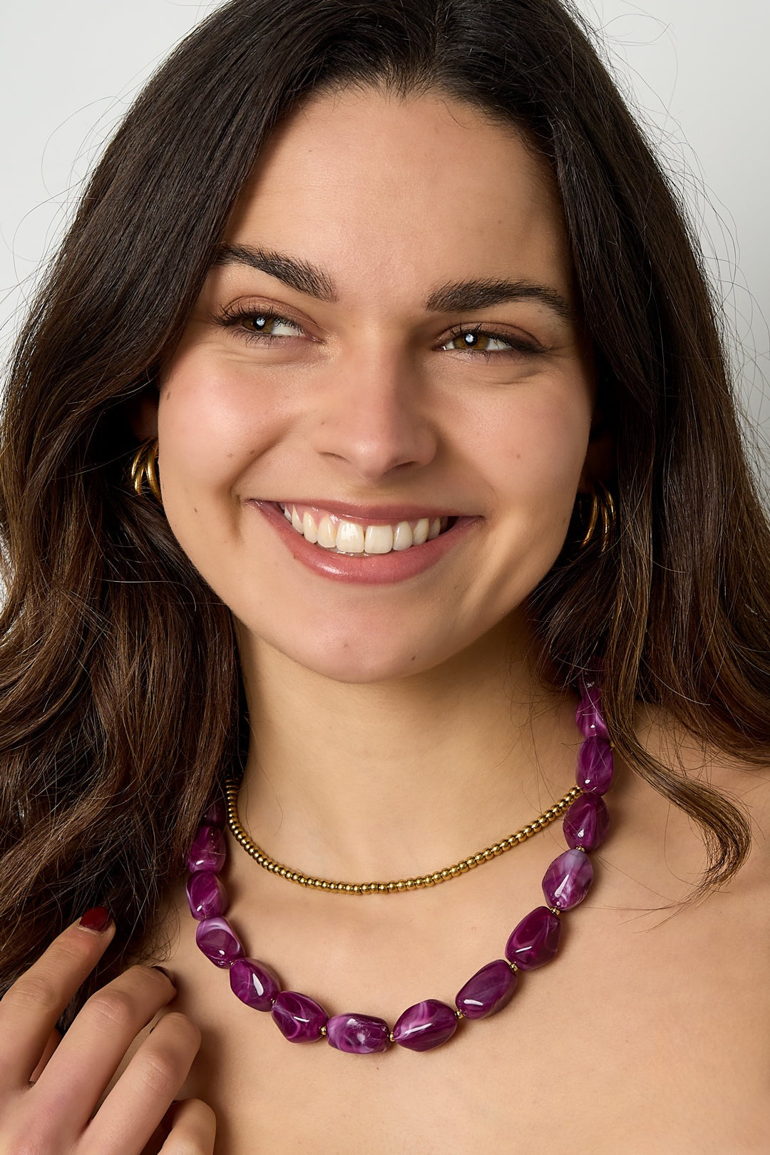Close-up of woman smiling wearing deep purple beaded necklace paired with gold ball chain necklace