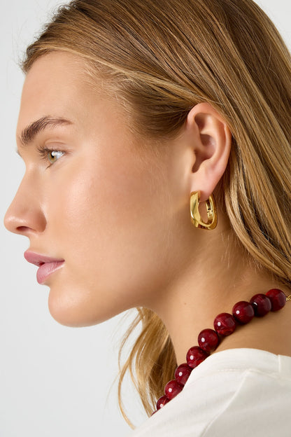 Model wearing gold twist rectangular hoop earrings with side profile and red bead necklace