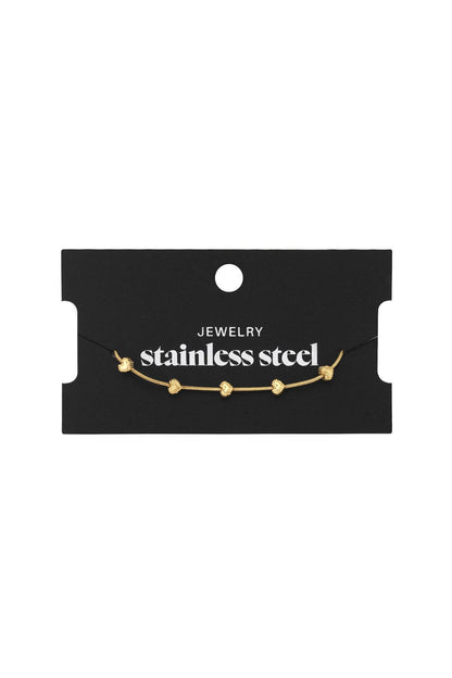 Gold-tone stainless steel bangle featuring delicate heart charms on a thin chain, displayed on black packaging.