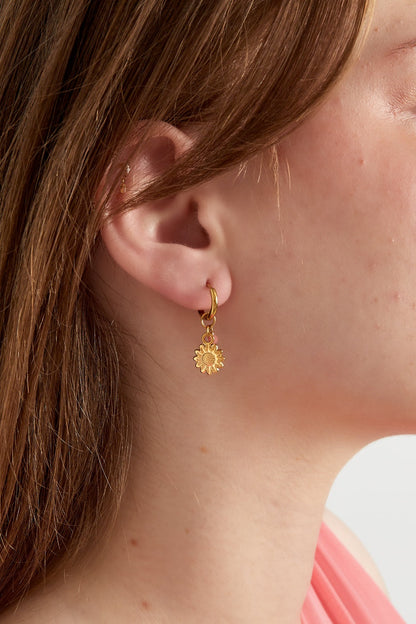 Close-up of a woman's ear wearing gold hoop earring with sunflower charm and pink bead, showcasing the fit and design