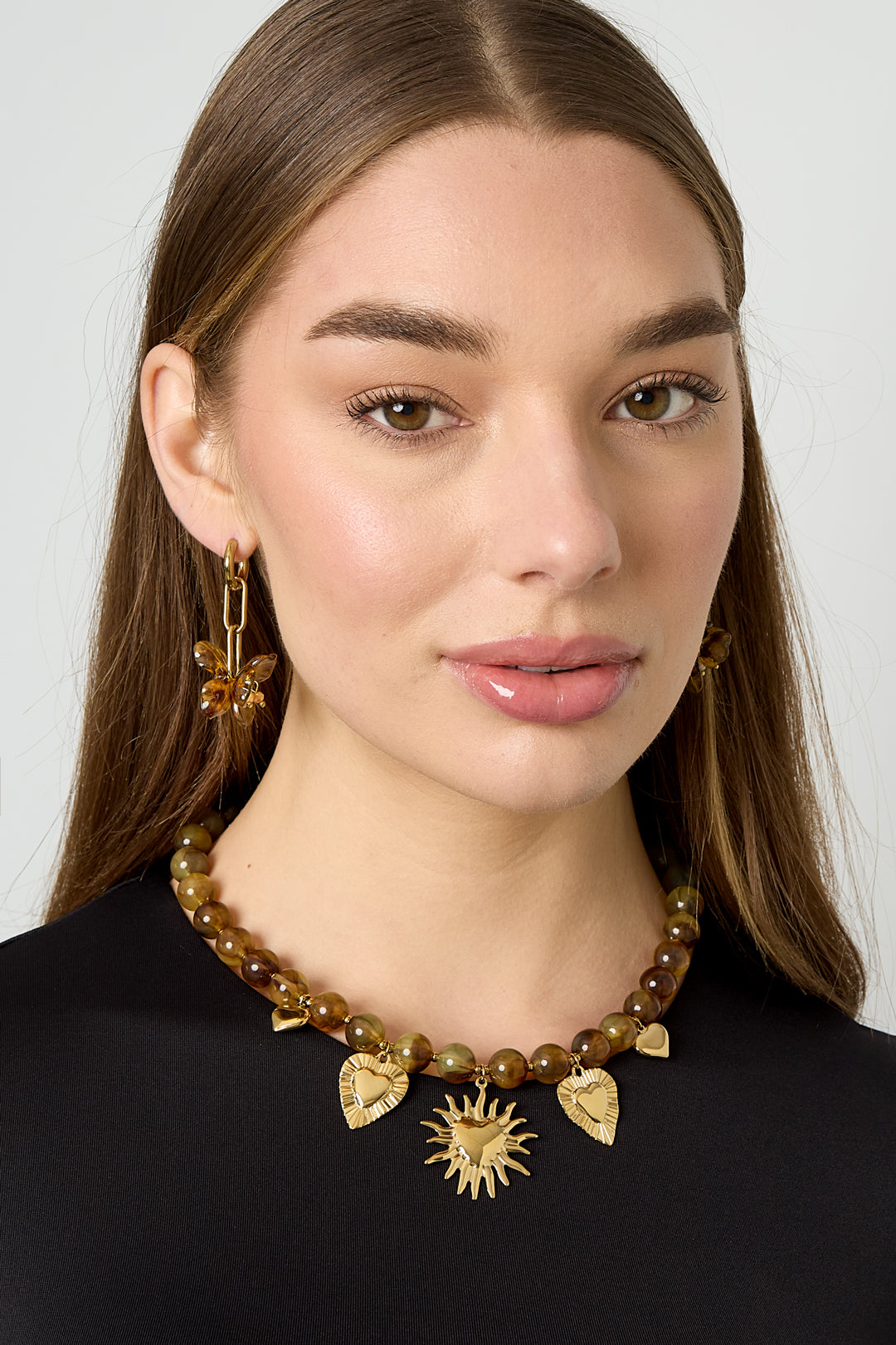 Model wearing amber brown beaded necklace with gold sun and heart charms paired with matching amber butterfly earrings