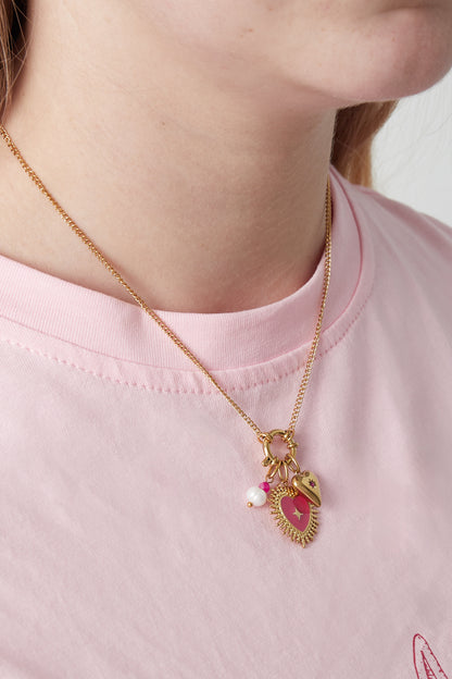 Gold pendant necklace with red enamel heart, pearl and pink flower charms worn over pink t-shirt