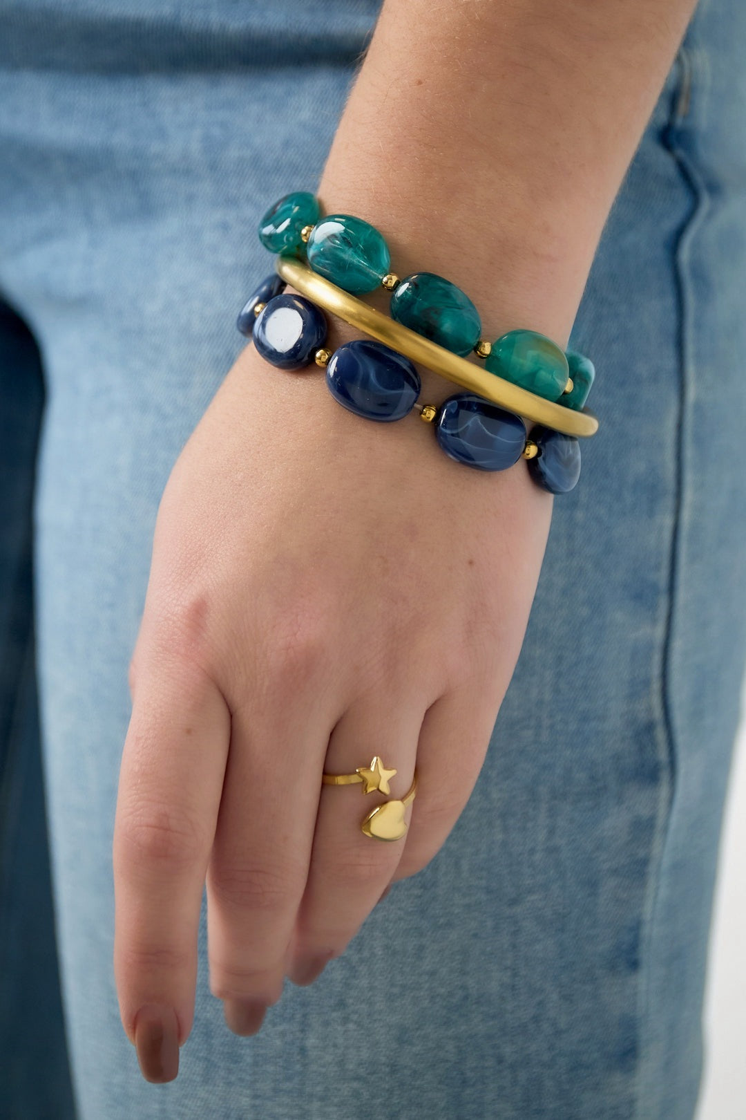 Model wearing stacked green and navy acrylic beaded bracelets and a gold heart star ring with jeans