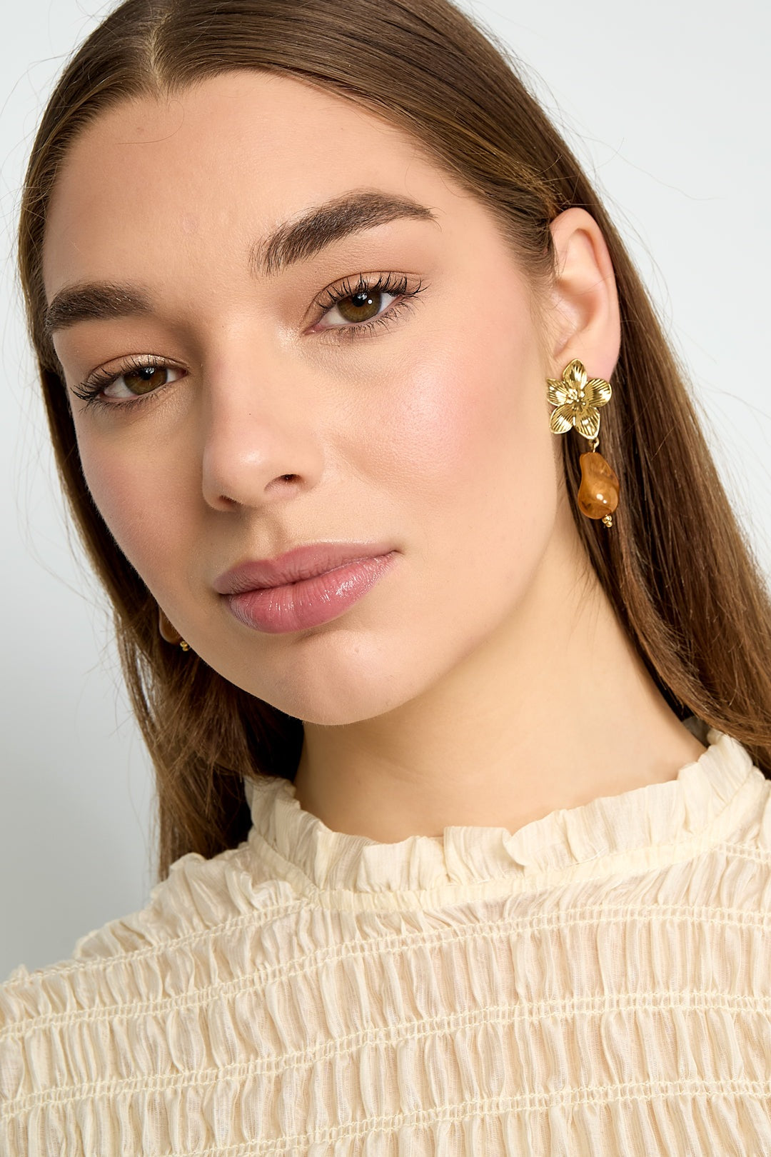 Side angle close-up of model's face wearing gold flower drop earring with amber bead