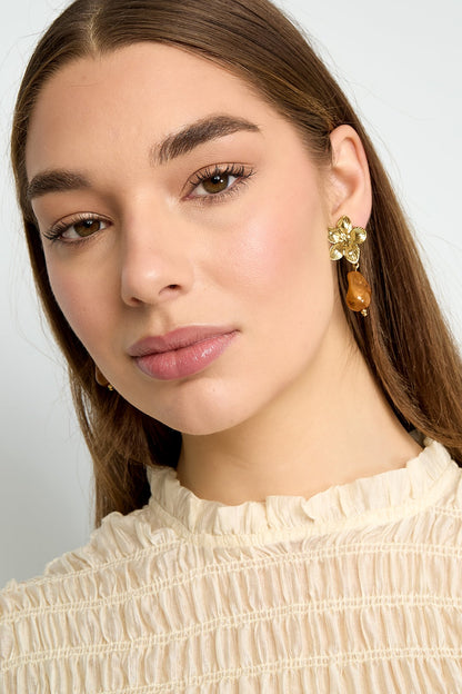 Side angle close-up of model's face wearing gold flower drop earring with amber bead