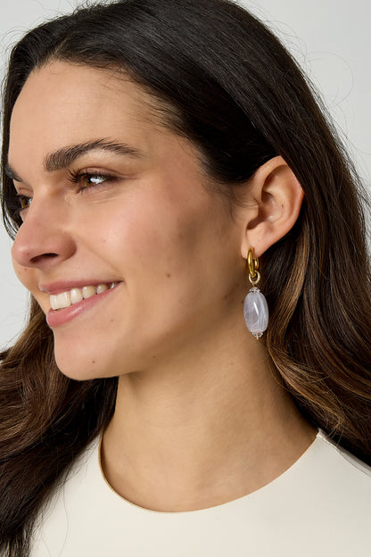 Model wearing gold hoop earrings with light lavender cloudy resin beads