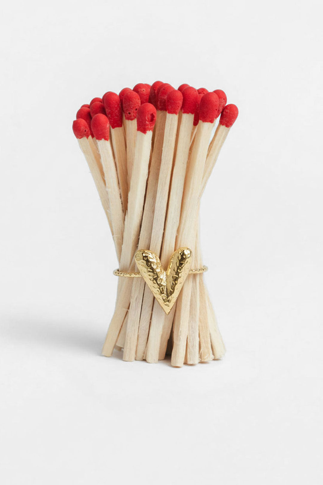 Hammered gold-tone heart ring resting on a bundle of matchsticks highlighting its texture and minimal vibe