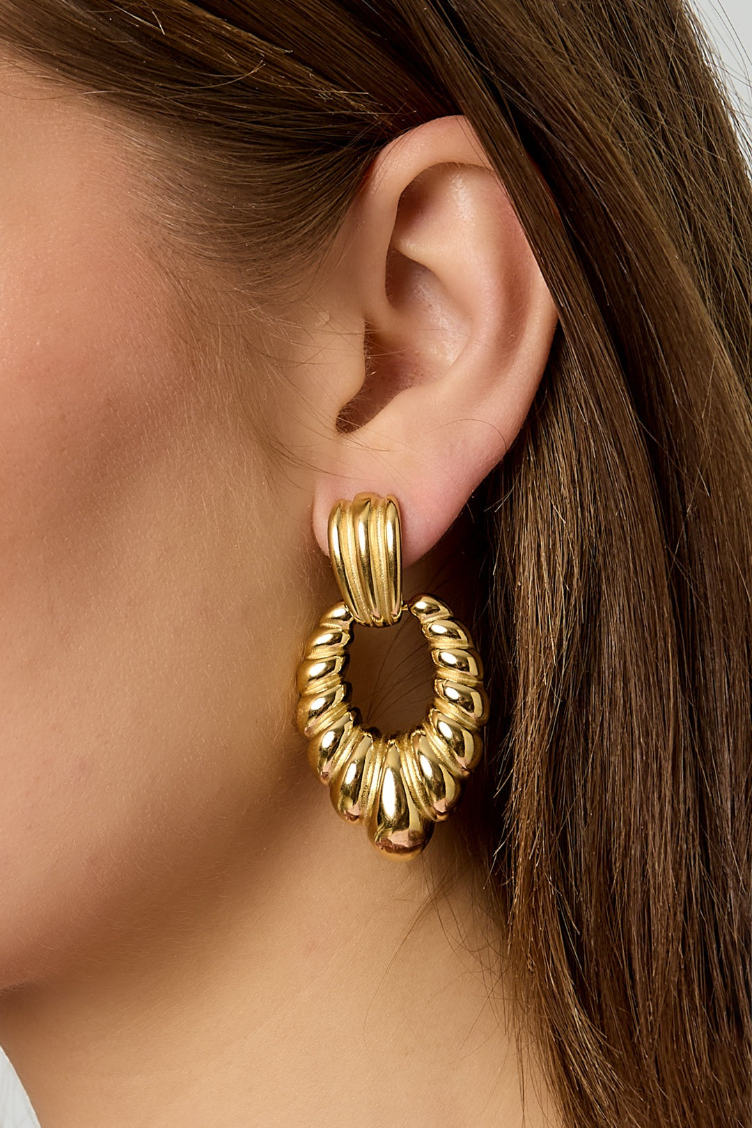 Close-up image focusing on one twisted gold hoop earring worn by the model