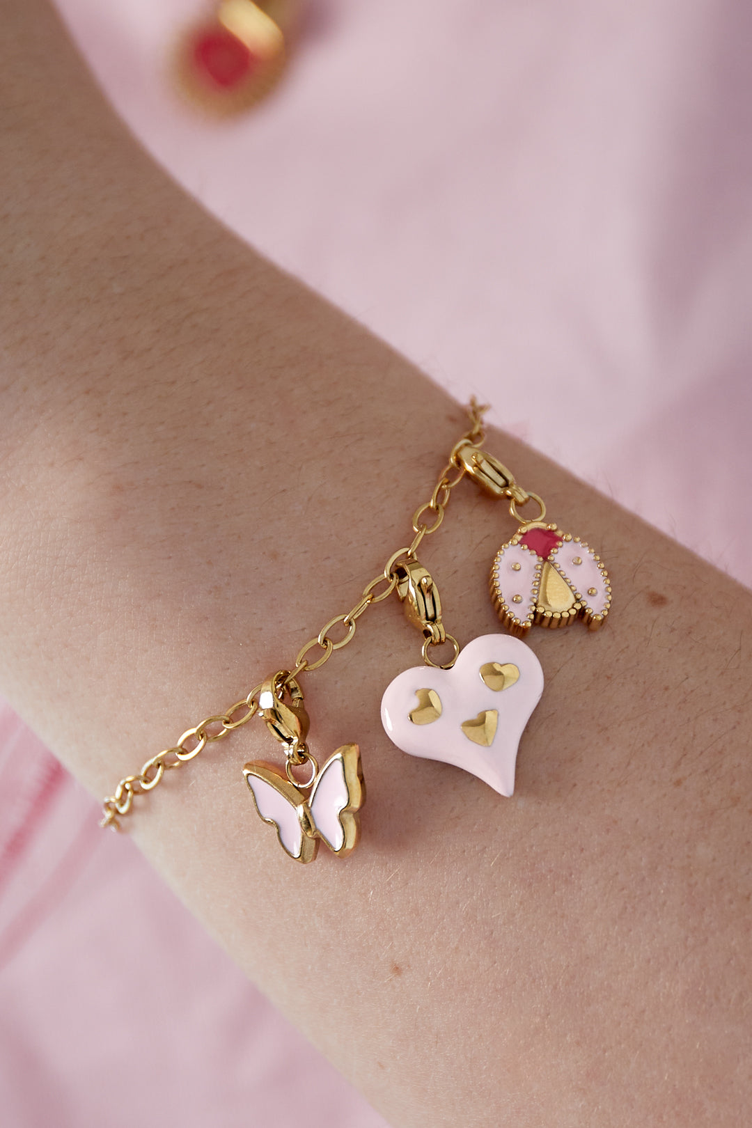 Close up of gold chain charm bracelet worn on wrist with pink heart, butterfly, and ladybug charms