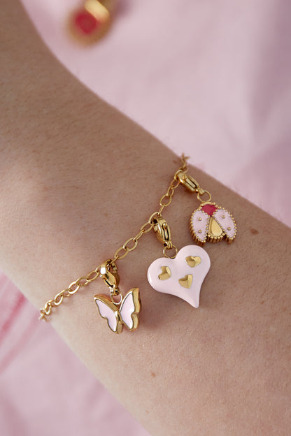 Close up of gold chain charm bracelet worn on wrist with pink heart, butterfly, and ladybug charms