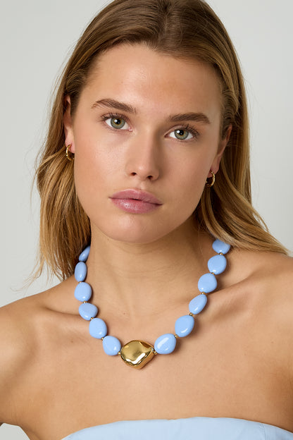 Model wearing sky blue beaded necklace with gold-tone centerpiece, styled with strapless light blue top