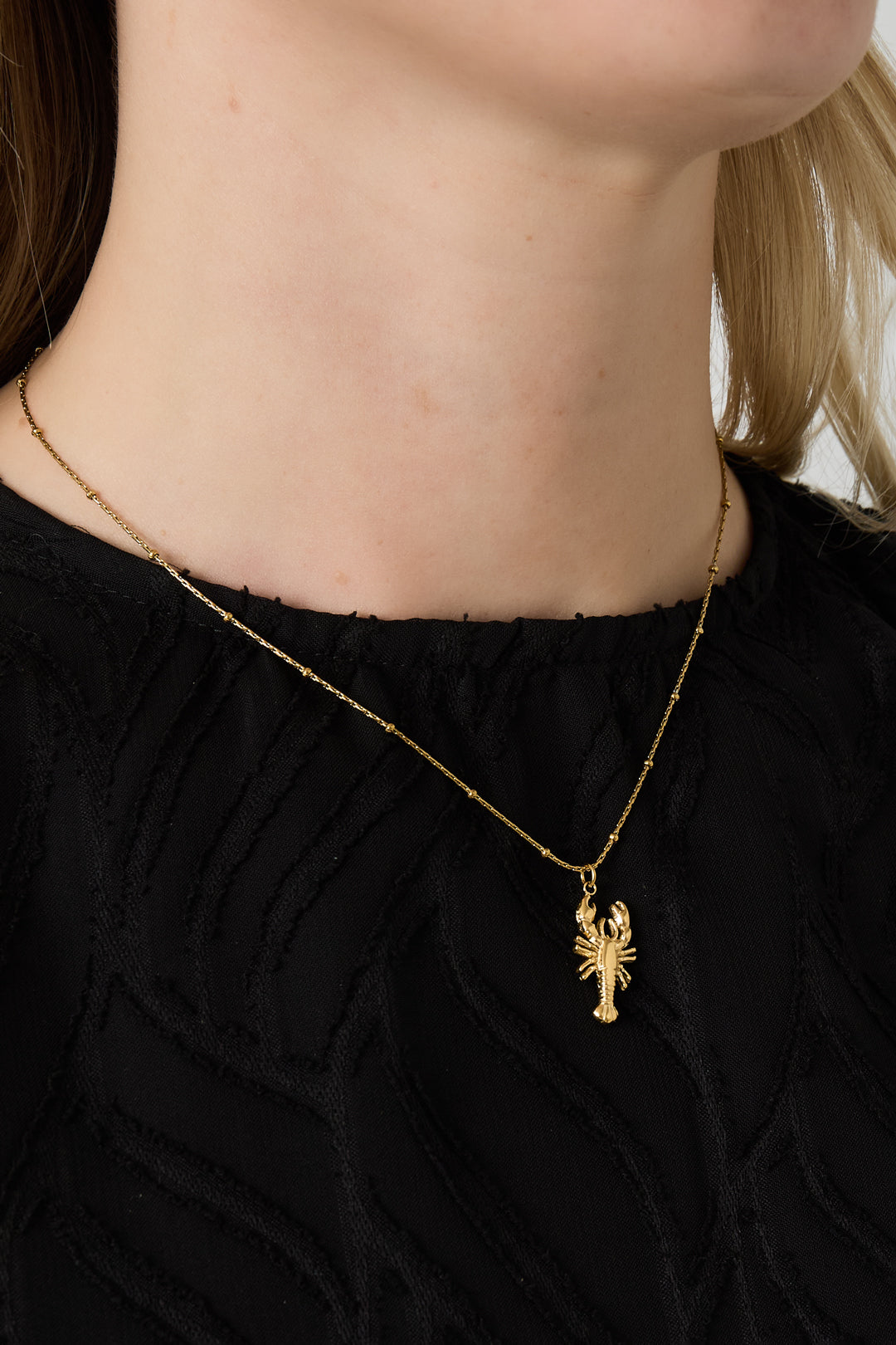 Close-up of woman wearing gold lobster pendant necklace with black textured top