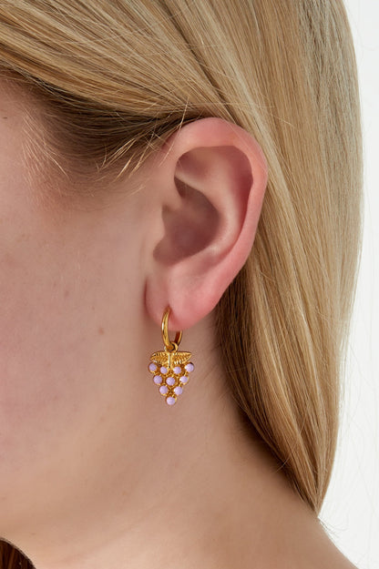 Close-up of gold grape drop earring with pastel pink enamel worn on a woman's ear