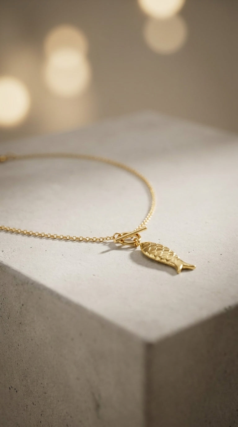 Gold Catching Vibes necklace featuring a textured, fish-shaped charm on a dainty chain with a toggle clasp.