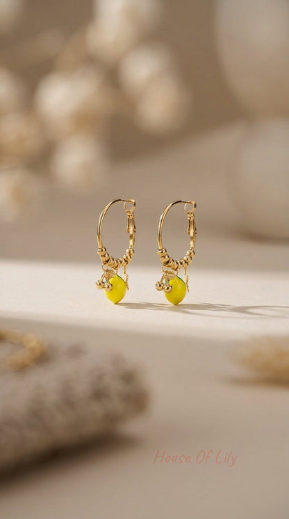Gold hoop earrings with beaded detailing and dangling charms of bright yellow lemons, set against a soft beige background.