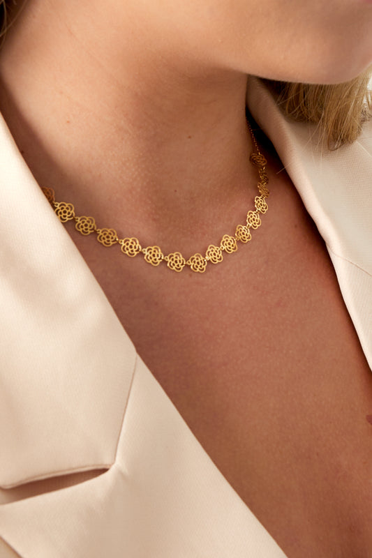 Model wearing the gold floral chain necklace styled with a cream blazer showing delicate charm details