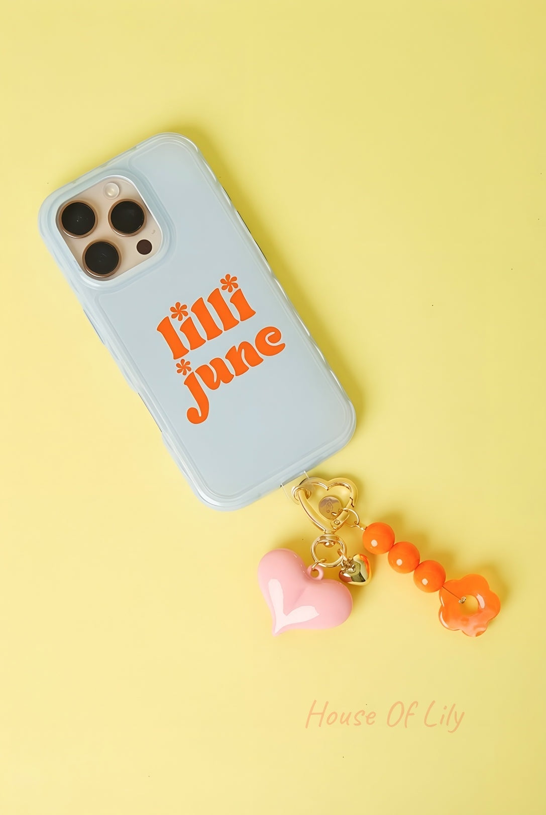 Pink heart acrylic bag charm with orange beads and flower accessory attached to a phone case on yellow background