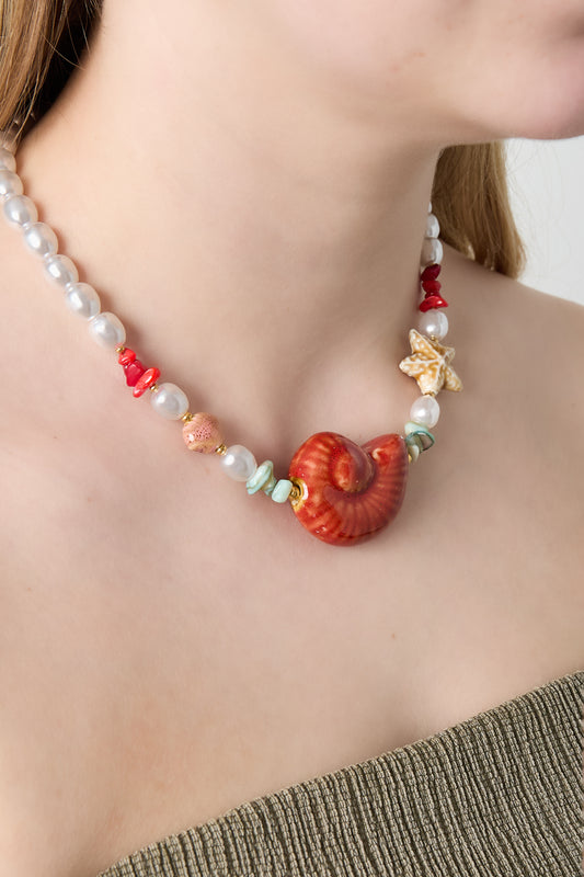 Model wearing the seashell pearl beaded necklace showcasing its vibrant red seashell center and colorful beads against bare skin and olive green strap top