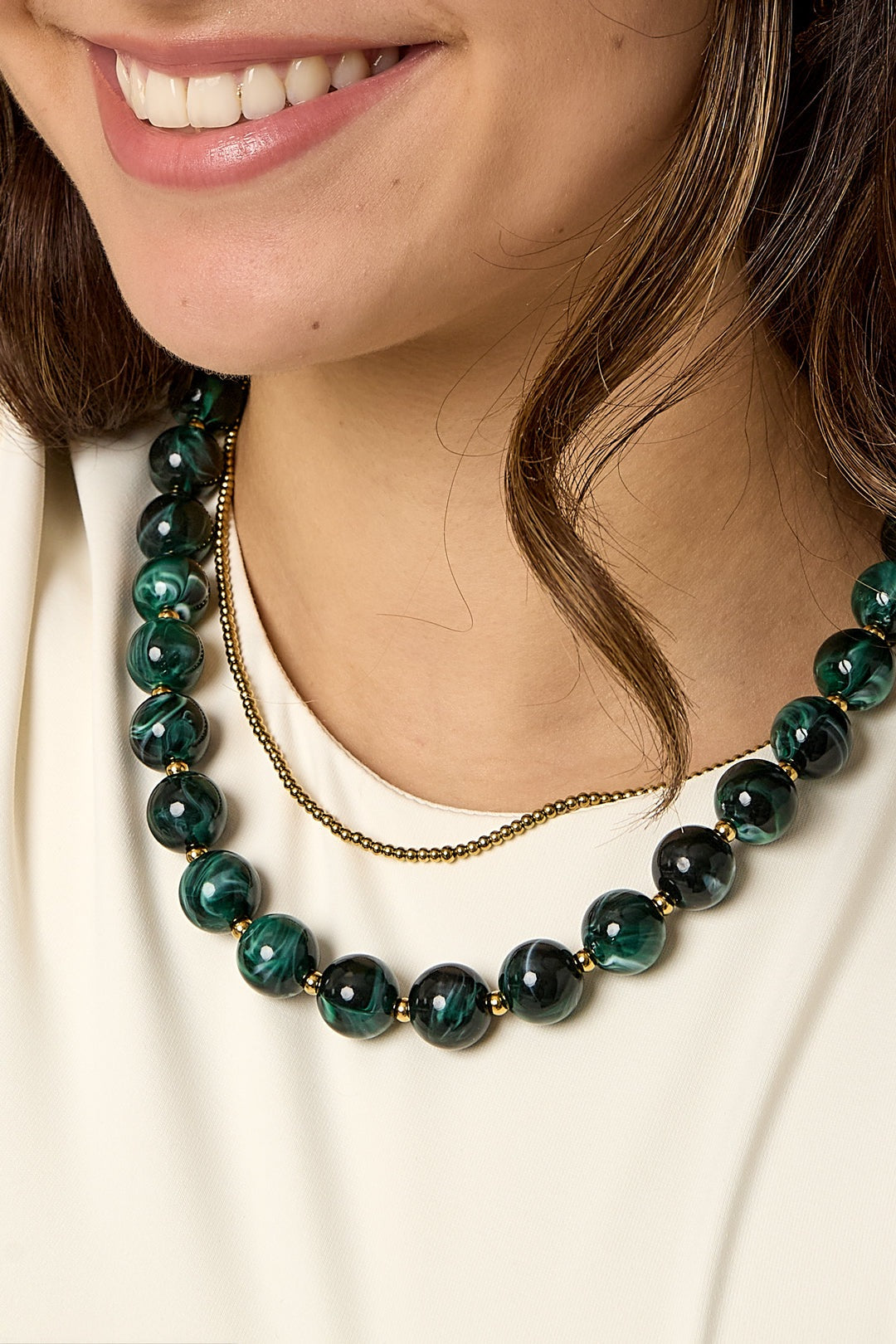 Close-up detail of green marbled statement necklace with gold spacer beads on woman wearing cream top