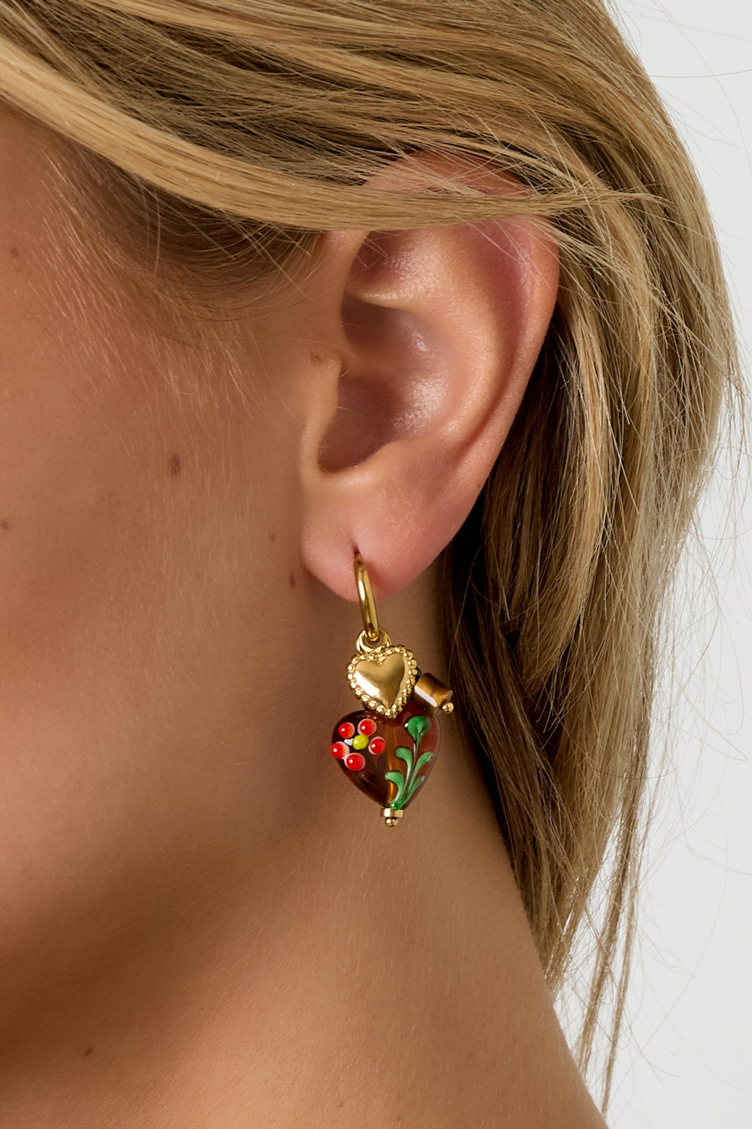 Close-up side view of woman wearing gold hoop earrings with brown floral heart charms showing detailed design